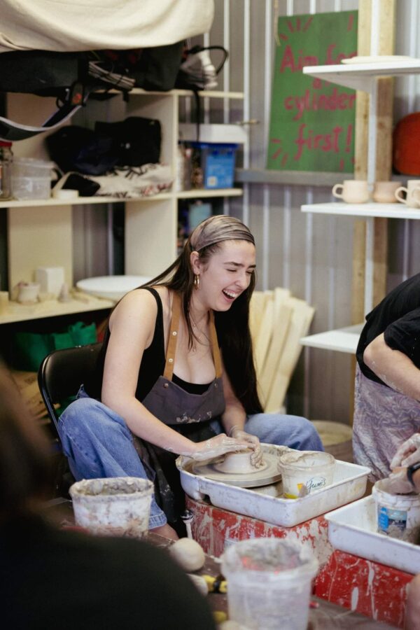 a woman sitting at a table making a clay bowl