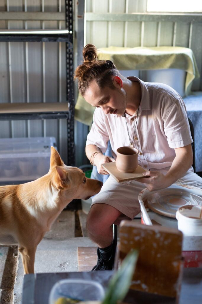 a person sitting on a chair and holding a small ceramic bowl with a dog
